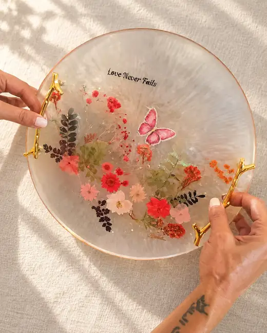 Her finished round tray, lettered Love never fails above pressed flowers and a butterfly, held in two hands